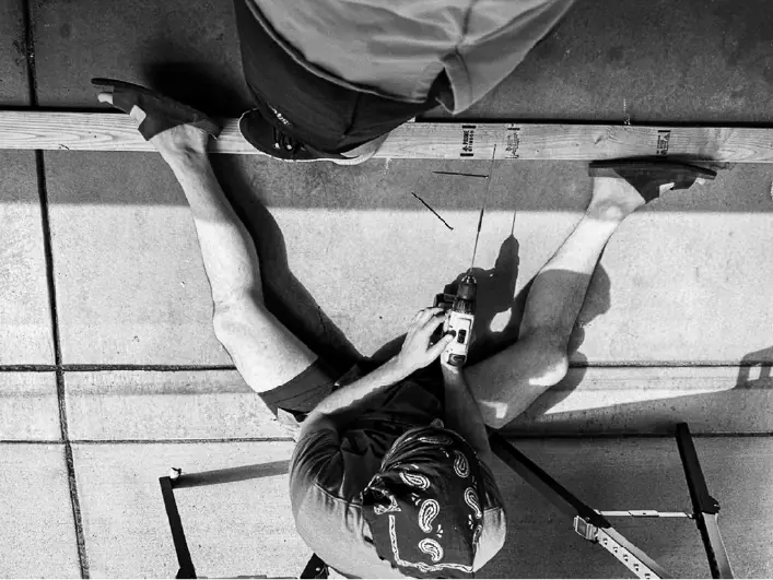 Overhead view of two people drilling a timber frame together on a garage floor.