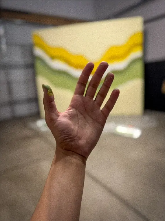 A paint-covered hand held up in front of the half-painted set wall.